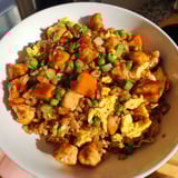Steaming plate of savory chicken fried rice, garnished with fresh green onions; a complete meal.