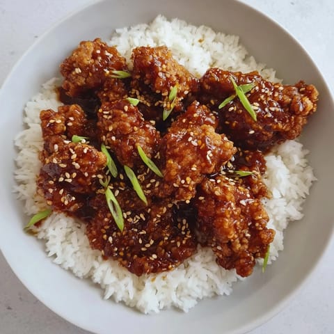 A vibrant photo of golden-brown General Tso's Chicken, with a scattering of green onions on top.