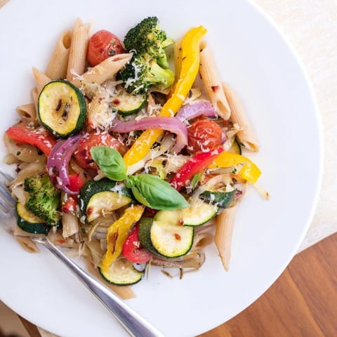 Golden roasted vegetables and al dente Pasta Primavera are garnished with fresh basil and lemon wedges on a rustic wooden table.  