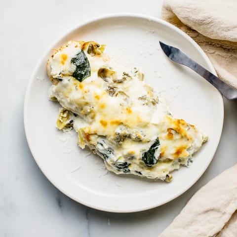 Golden-brown spinach and artichoke chicken bake in a ceramic dish, bubbling with creamy cheese and tender baked chicken breasts.
