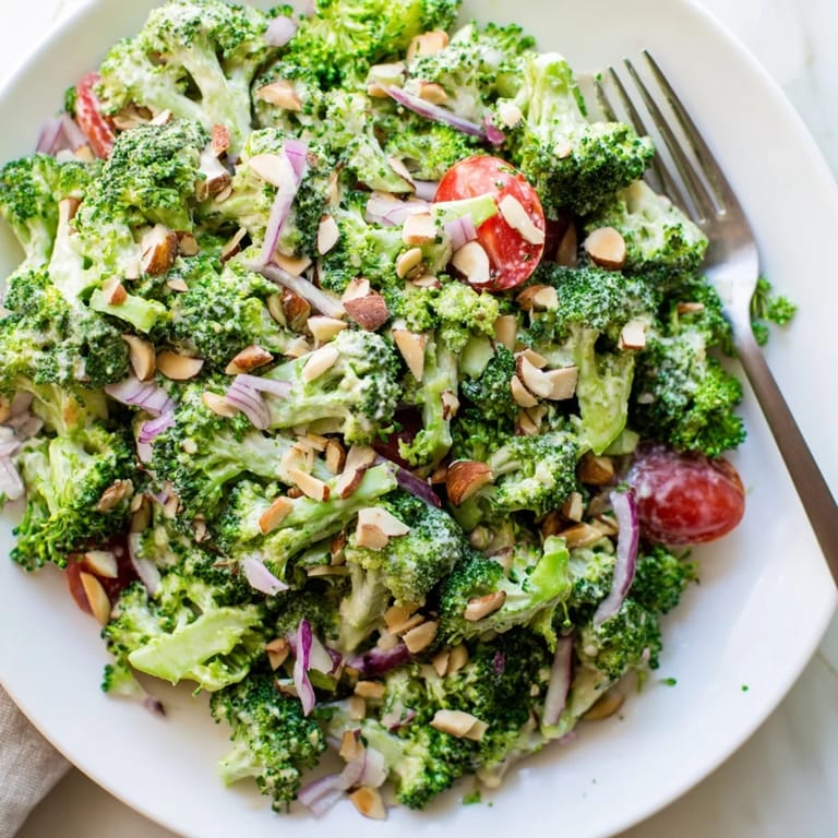 Freshly blanched broccoli mixed with red onion and cherry tomatoes in a tangy, creamy garlic-Parmesan dressing, ready to enjoy.